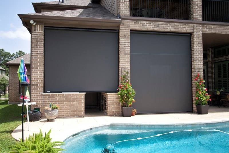 Two side-by-side motorized retractable window screens face-mounted on brick home