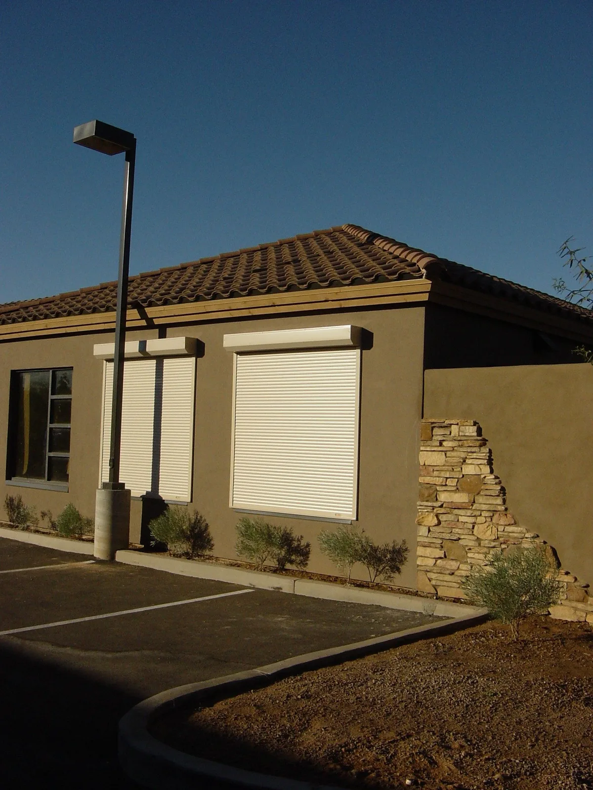 Tan stucco commercial building with cream metal rolling shutters closed for storm and wind protection