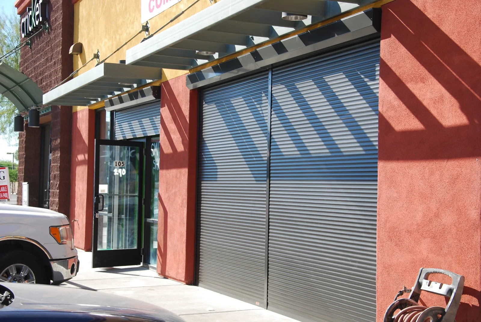 Storefront with metal rolling shutters closed across glass doors, blocking UV rays and direct sunlight