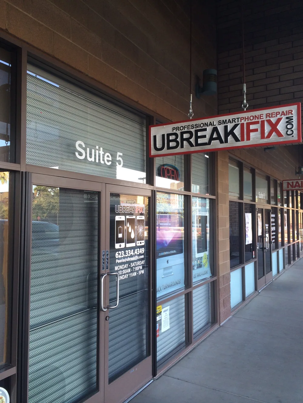 Phone repair storefront with vertical security mesh shutters protecting the glass entrance and side windows
