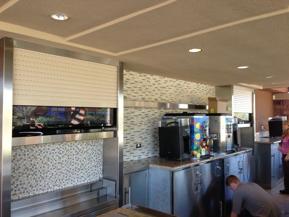 White roll-down counter shutter closed over a stainless steel beverage and concession station inside a restaurant
