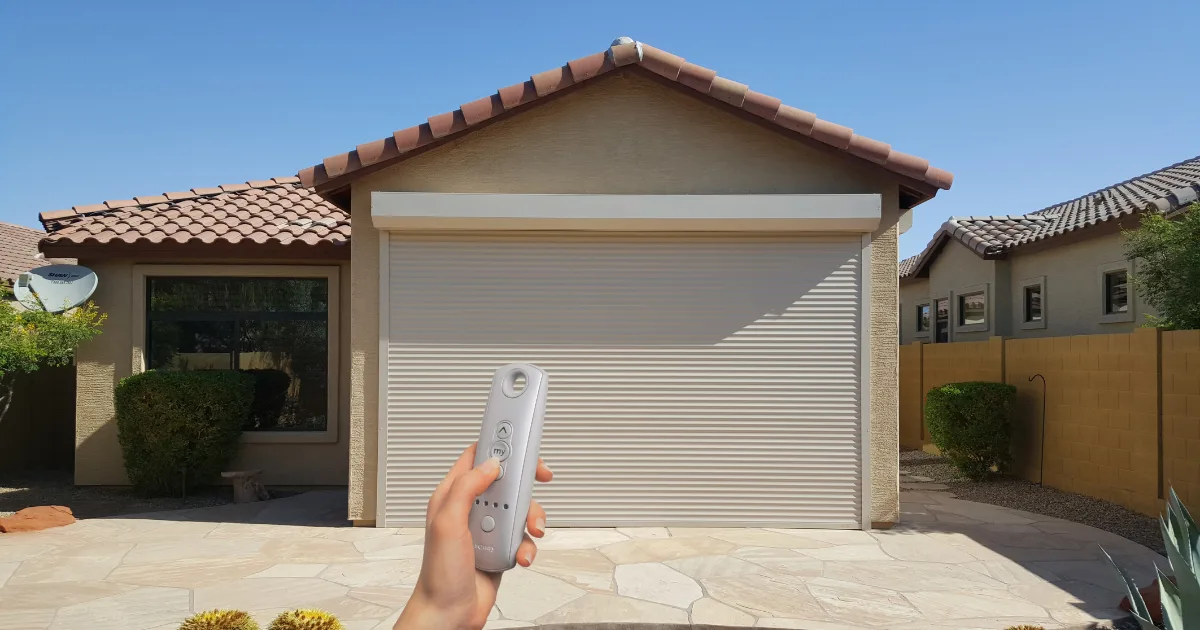 Hand holding a Roll-A-Shield remote control in front of a closed 38mm insulated rolling shutter garage door
