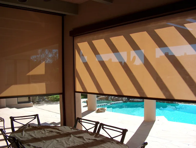 Tan rolling screens lowered over a covered patio dining area beside a Phoenix pool