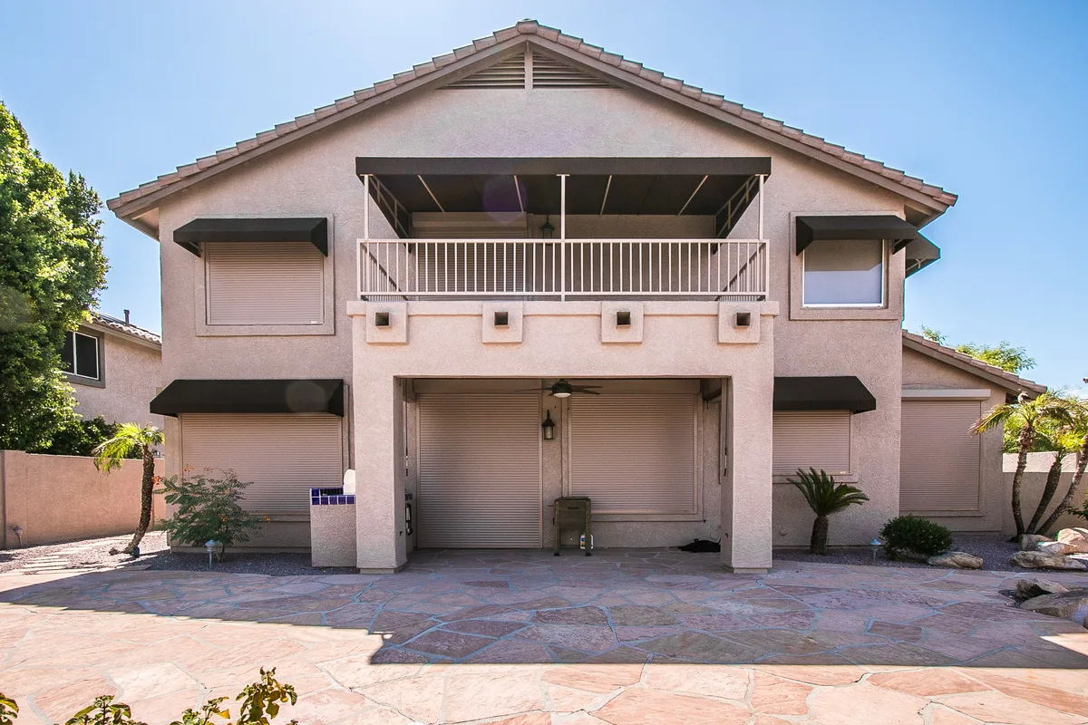 Two-story Phoenix home with tan rolling shutters closed over every window and patio opening