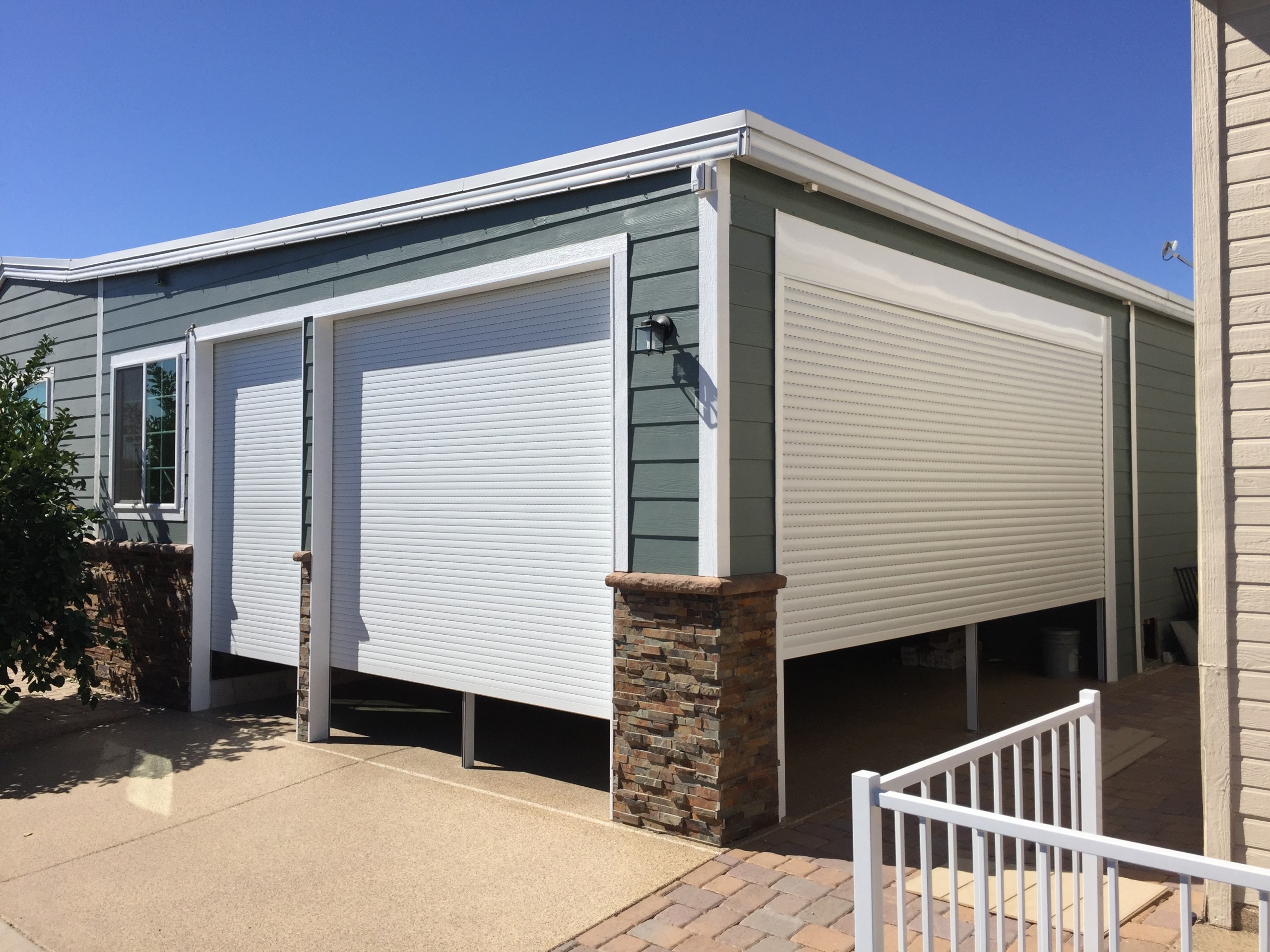 Rolling shutters part way down across garage and carport openings with the guide rails running down each side