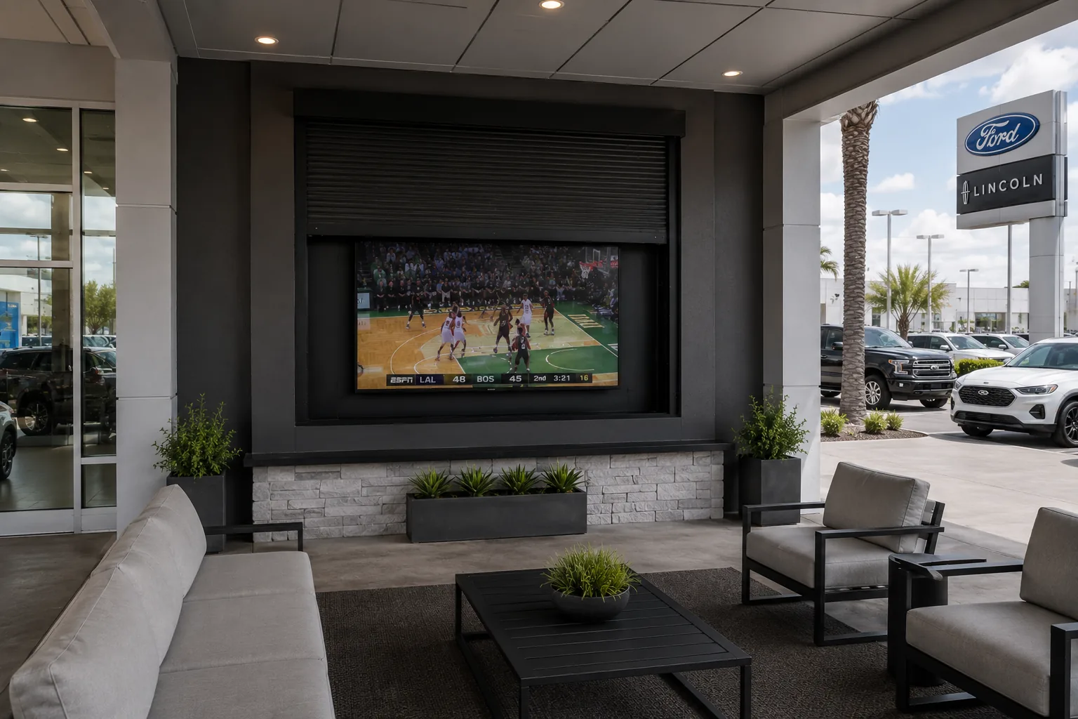 Black rolling shutter partly lowered over an outdoor television built into a wall in a covered commercial lounge