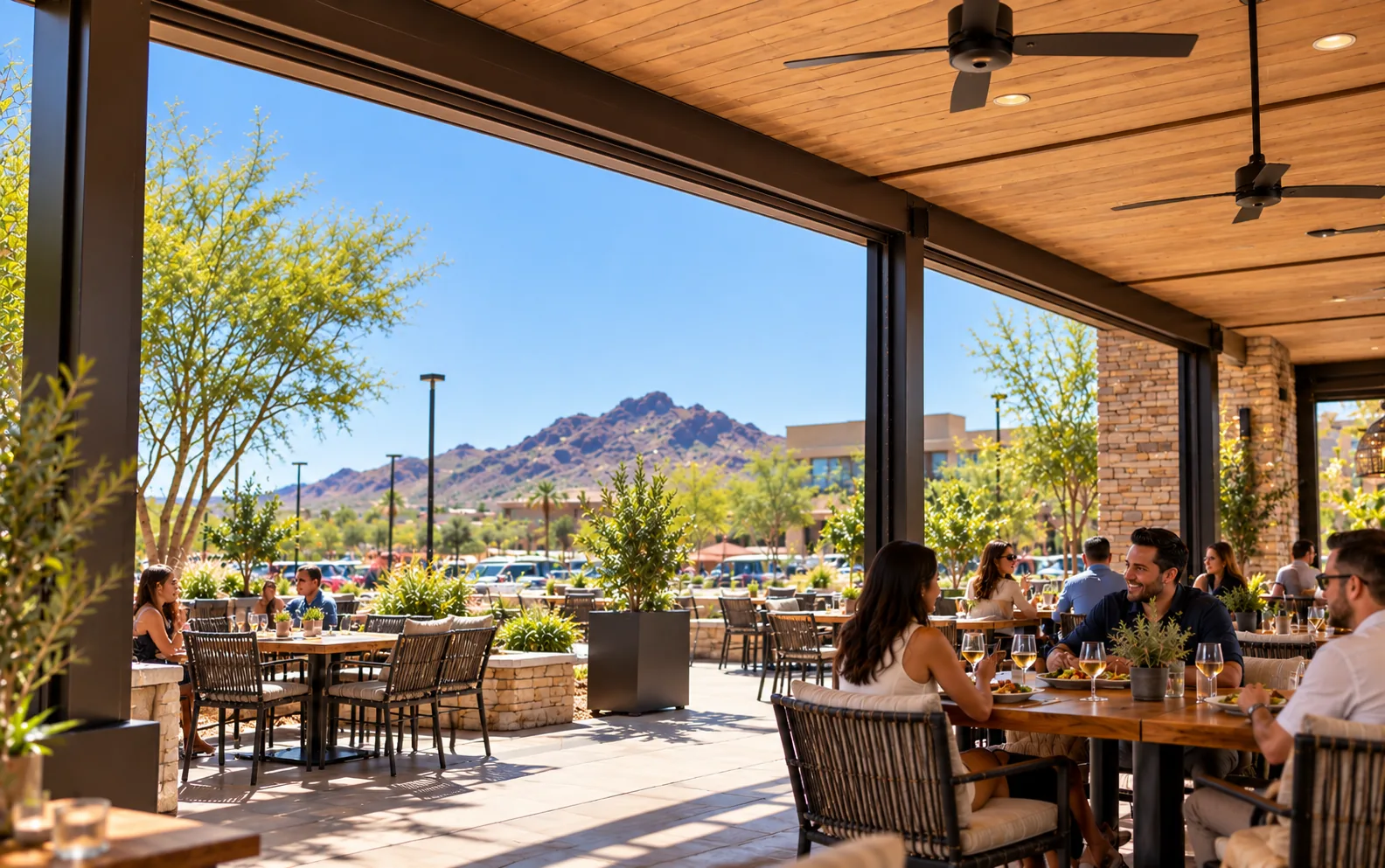 Covered restaurant patio with screens fully retracted into slim housings under the beam, opening the view to desert mountains and a clear blue sky