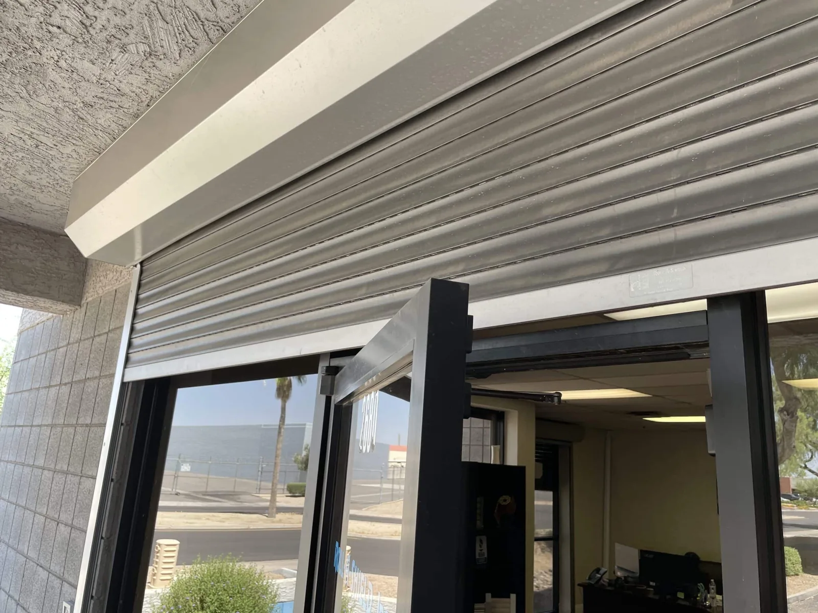 Rolling shutter stopped partway down above an open glass door at a commercial entrance