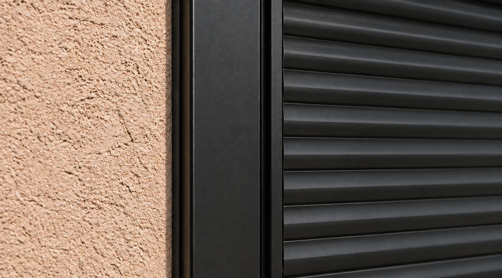Close-up of a black aluminum guide rail with the rolling shutter slats seated in its track against a stucco wall